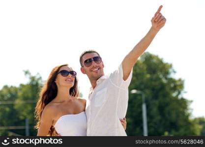 love, travel, tourism, people and friendship concept - smiling couple wearing sunglasses hugging and pointing finger in park