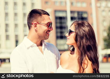 love, travel, tourism, people and friendship concept - smiling couple wearing sunglasses looking at each other in city