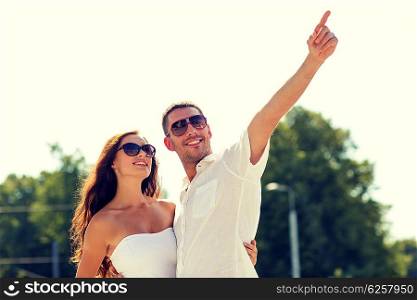 love, travel, tourism, people and friendship concept - smiling couple wearing sunglasses hugging and pointing finger in park