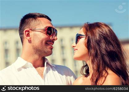 love, travel, tourism, people and friendship concept - smiling couple wearing sunglasses looking at each other in city