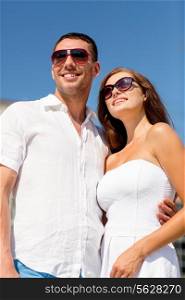 love, travel, tourism, people and friendship concept - smiling couple wearing sunglasses hugging in city