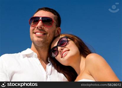 love, travel, tourism, people and friendship concept - smiling couple wearing sunglasses over blue sky background