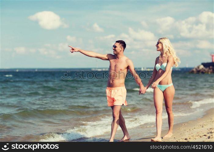 love, travel, tourism, summer and people concept - smiling couple on vacation in swimwear and sunglasses holding hands and walking on beach