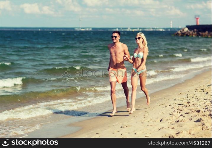 love, travel, tourism, summer and people concept - smiling couple on vacation in swimwear and sunglasses holding hands and running on beach