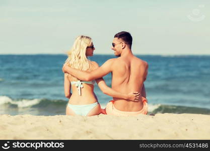love, travel, tourism, summer and people concept - smiling couple on vacation in swimwear sitting and hugging on beach from back