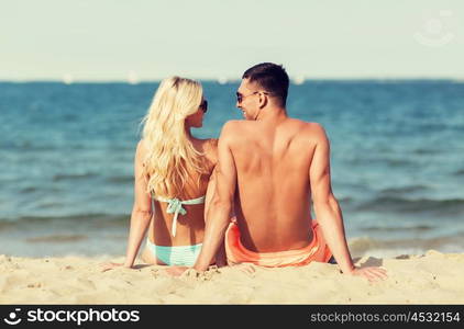 love, travel, tourism, summer and people concept - smiling couple on vacation in swimwear sitting on beach from back