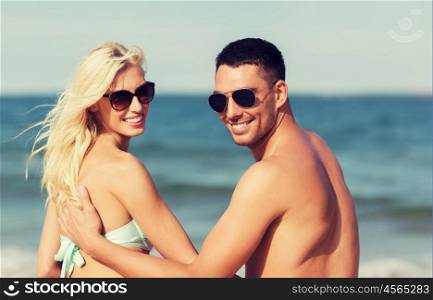 love, travel, tourism, summer and people concept - smiling couple on vacation in swimwear sitting on beach and looking back