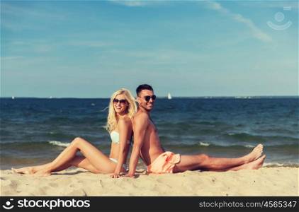 love, travel, tourism, summer and people concept - smiling couple on vacation in swimwear sitting on beach back to back. happy couple in swimwear sitting on summer beach