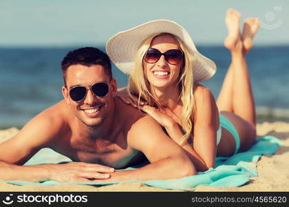 love, travel, tourism, summer and people concept - smiling couple on vacation in swimwear and sunglasses sunbathing on beach