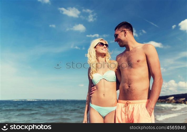 love, travel, tourism, summer and people concept - smiling couple on vacation in swimwear and sunglasses holding hands and walking on beach
