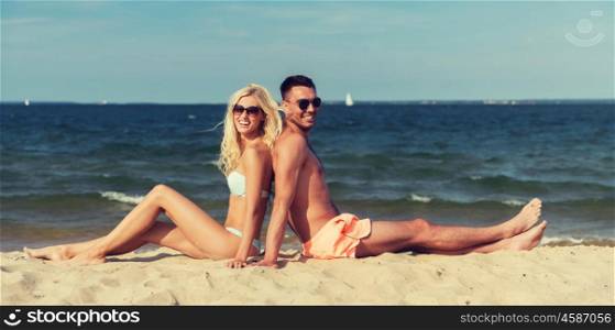 love, travel, tourism, summer and people concept - smiling couple on vacation in swimwear sitting on beach back to back