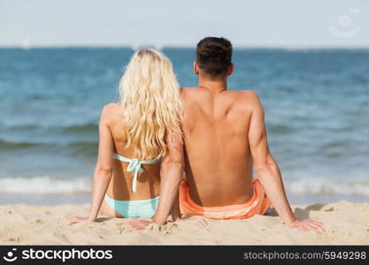 love, travel, tourism, summer and people concept - smiling couple on vacation in swimwear sitting on beach from back