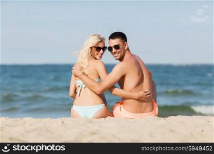 love, travel, tourism, summer and people concept - smiling couple on vacation in swimwear sitting on beach and looking back