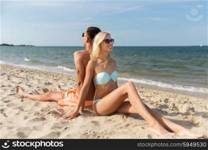 love, travel, tourism, summer and people concept - smiling couple on vacation in swimwear sitting on beach back to back