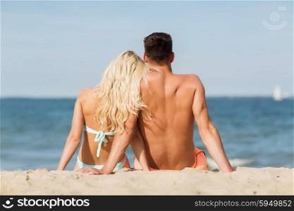 love, travel, tourism, summer and people concept - smiling couple on vacation in swimwear sitting on beach from back