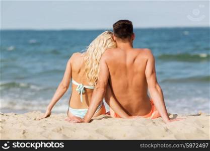 love, travel, tourism, summer and people concept - smiling couple on vacation in swimwear sitting on beach from back