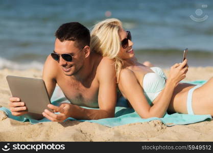 love, travel, tourism, technology and people concept - happy couple on vacation with tablet pc computer sunbathing on summer beach