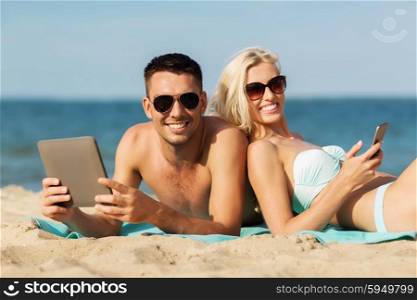 love, travel, tourism, technology and people concept - happy couple on vacation with tablet pc computer sunbathing on summer beach