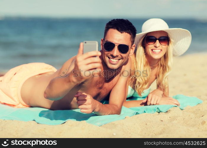 love, travel, tourism, technology and people concept - smiling couple on vacation in swimwear and sunglasses and taking selfie with smartphone on summer beach