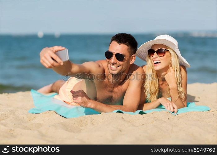 love, travel, tourism, technology and people concept - smiling couple on vacation in swimwear and sunglasses and taking selfie with smartphone on summer beach