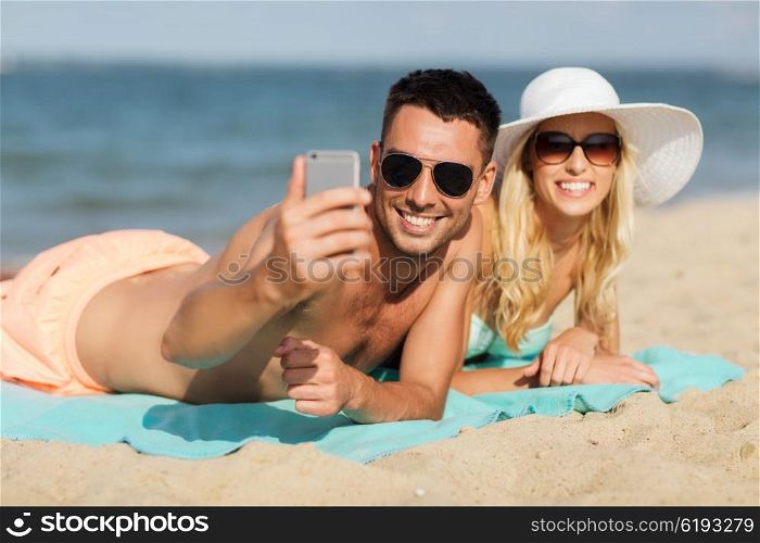 love, travel, tourism, technology and people concept - smiling couple on vacation in swimwear and sunglasses and taking selfie with smartphone on summer beach