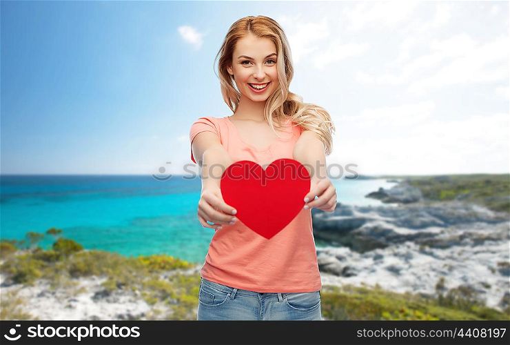 love, travel, tourism, valentines day and people concept - smiling young woman or teenage girl with blank red heart shape over exotic tropical beach background