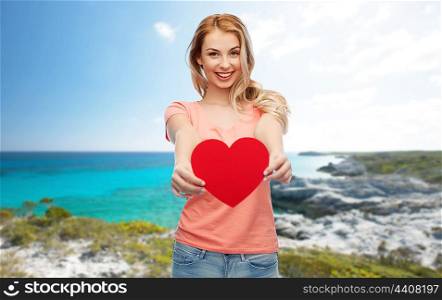 love, travel, tourism, valentines day and people concept - smiling young woman or teenage girl with blank red heart shape over exotic tropical beach background