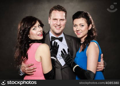 Love triangle or friendship. Portrait of smiling two women and one man wearing elegant clothes on black. Luxury party.