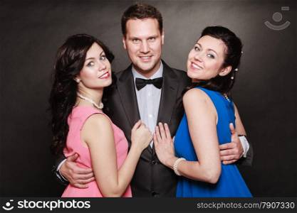 Love triangle or friendship. Portrait of smiling two women and one man wearing elegant clothes on black. Luxury party.