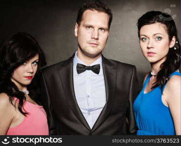 Love triangle. Portrait of two women and one man wearing elegant clothes on black. Mistress and betrayal within the family. Choice before wedding. Luxury party.