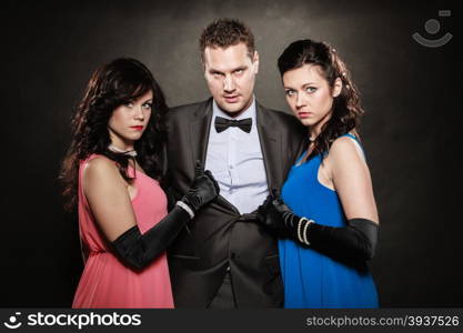 Love triangle. Portrait of two women and one man wearing elegant clothes on black. Mistress and betrayal within the family. Choice before wedding. Luxury party.