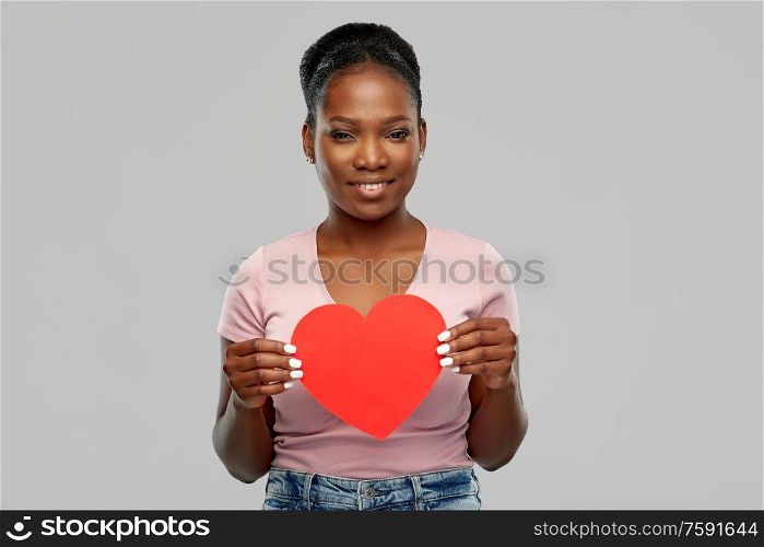 love, valentine&rsquo;s day and charity concept - happy african american young woman with red heart over grey background. happy african american woman with red heart
