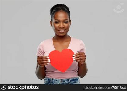 love, valentine&rsquo;s day and charity concept - happy african american young woman with red heart over grey background. happy african american woman with red heart