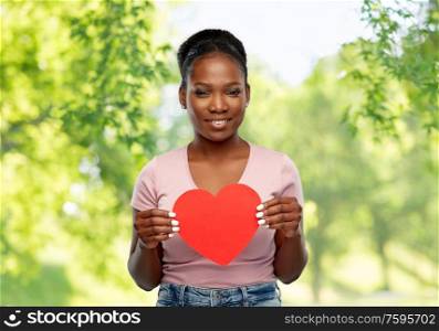 love, valentine&rsquo;s day and charity concept - happy african american young woman with red heart over green natural background. happy african american woman with red heart