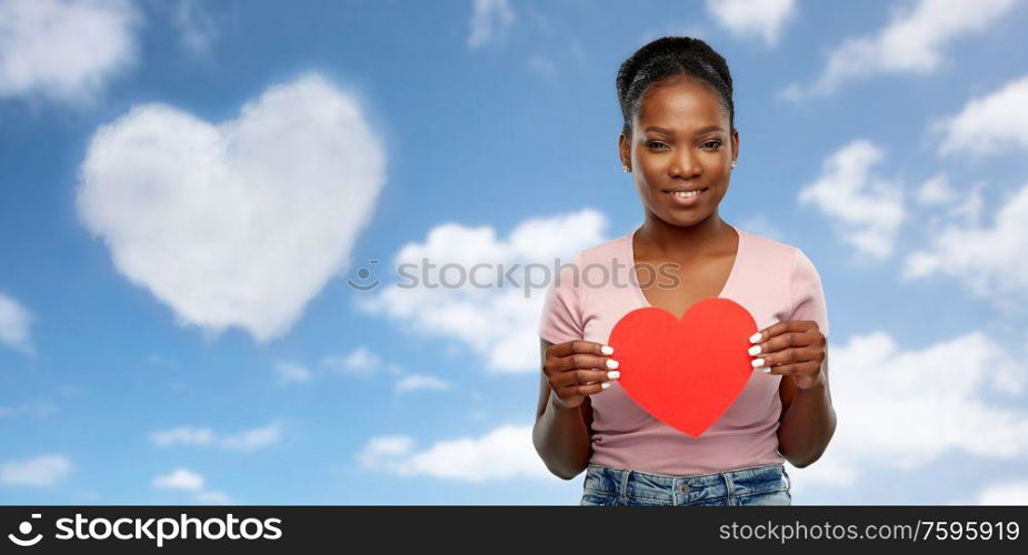 love, valentine&rsquo;s day and charity concept - happy african american young woman with red heart over grey background. happy african american woman with red heart