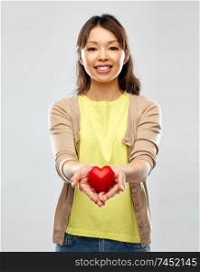 love, valentine&rsquo;s day and charity concept - happy asian young woman holding red heart over grey background. happy asian woman holding red heart
