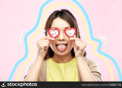 love, valentine&rsquo;s day and charity concept - happy young woman with red hearts instead of eyes showing tongue over pink background with glowing lines. happy woman with eyes of hearts