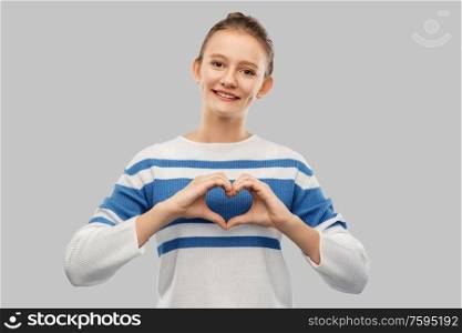 love, valentine&rsquo;s day and people concept - smiling teenage girl making hand heart gesture over grey background. smiling teenage girl making hand heart