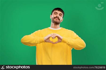 love, valentine&rsquo;s day and people concept - young man in yellow sweatshirt girl making hand heart gesture over emerald green background. young man in yellow sweatshirt l making hand heart