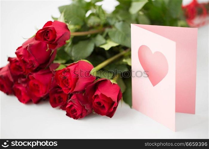 love, valentines day and holidays concept - close up of red roses bunch and greeting card with heart. close up of red roses and greeting card with heart