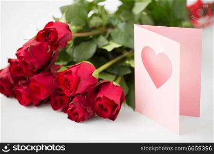love, valentines day and holidays concept - close up of red roses bunch and greeting card with heart. close up of red roses and greeting card with heart