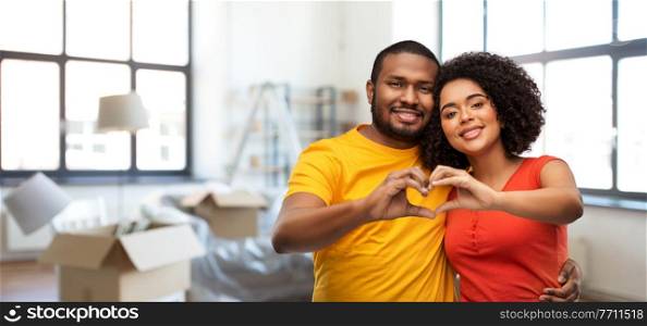 love, valentines day and moving concept - happy african american couple making hand heart gesture over new home background. happy couple making hand heart at new home