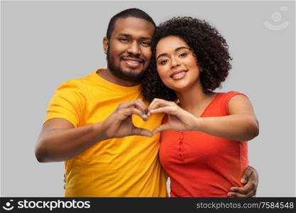 love, valentines day and people concept - happy african american couple making hand heart gesture over grey background. happy african american couple making hand heart