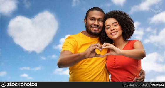 love, valentines day and people concept - happy african american couple making hand heart gesture over blue sky and clouds background. happy african american couple making hand heart