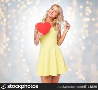 love, valentines day and people concept - smiling young woman in dress with red paper heart over holidays lights background. happy young woman with red paper heart