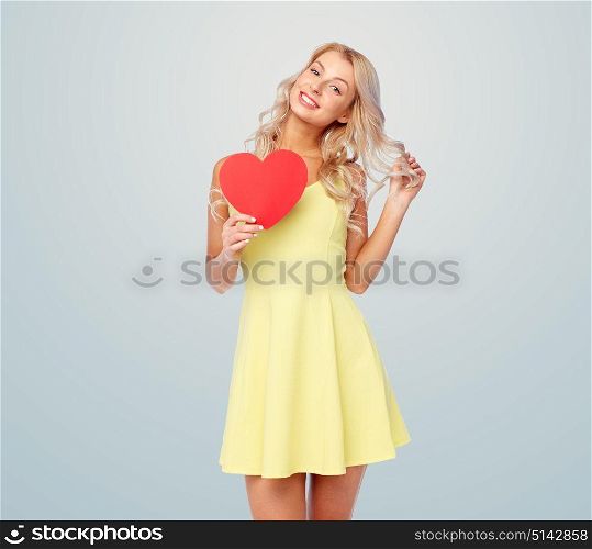 love, valentines day and people concept - smiling young woman in dress with red paper heart over gray background. happy young woman with red paper heart over gray