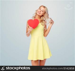 love, valentines day and people concept - smiling young woman in dress with red paper heart over gray background. happy young woman with red paper heart over gray