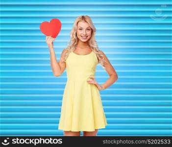 love, valentines day and people concept - smiling young woman in dress with red paper heart over ribbed blue background. happy young woman with red paper heart
