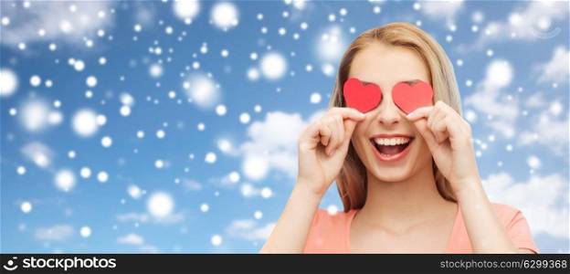 love, valentines day and people concept - smiling young woman or teenage girl with red heart shapes on eyes over blue sky background and snow. happy young woman with red heart shapes on eyes