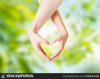love, valentines day and relationships concept - close up of couple hands showing heart gesture over green natural background. close up of couple hands showing heart gesture. close up of couple hands showing heart gesture